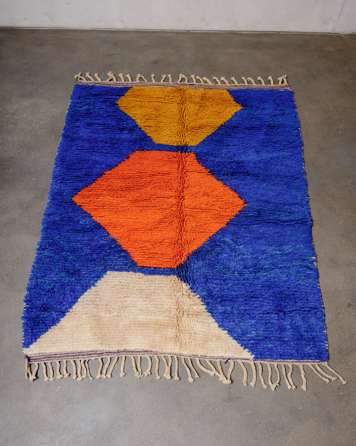 Berberlin vintage wool boujad rug in bold colours with natural wool tassels laying flat on concrete floor.